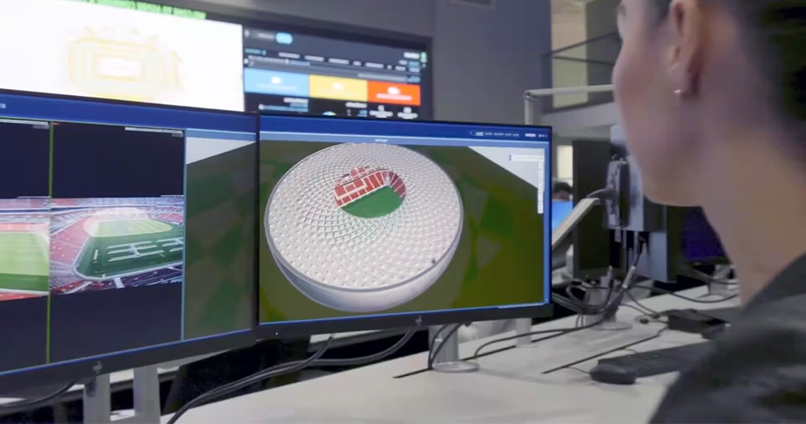 A person looking at a monitor displaying a 3D model of a stadium from the control room