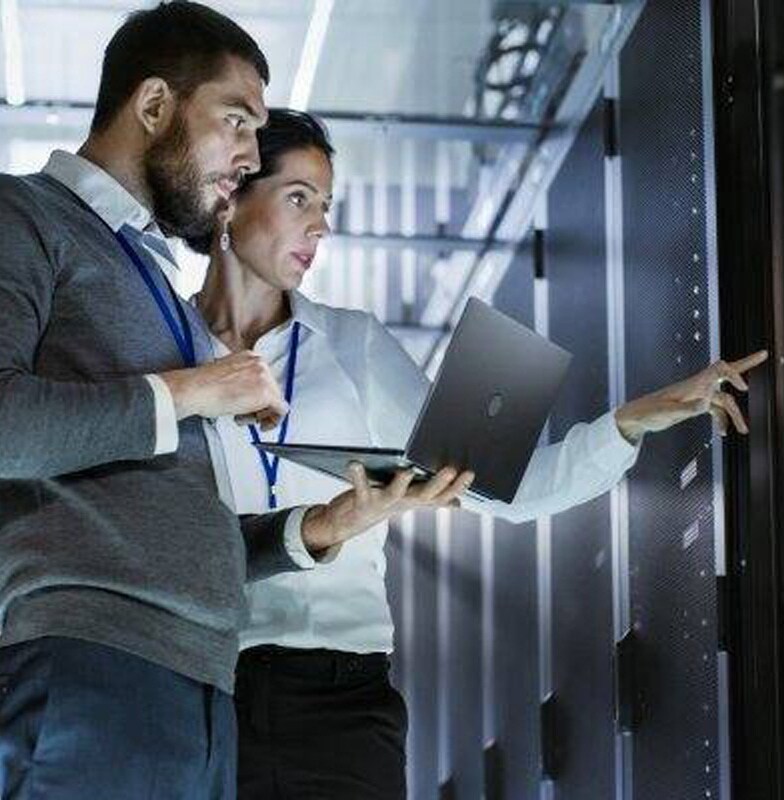 Two employees standing and discussing in the data center room while holding a laptop