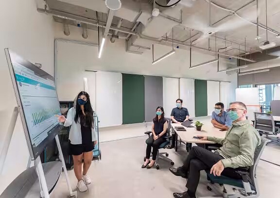 A group of employees wearing masks are in the conference room with one of employee presenting