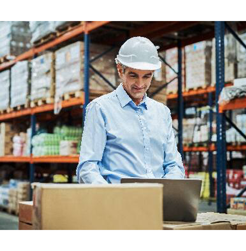 A warehouse worker  standing and working on his laptop 