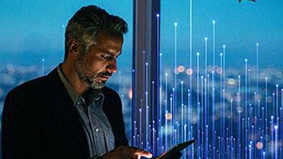 A person standing near the glass window and looking at the tab overlaid with graphics of transmission nodes