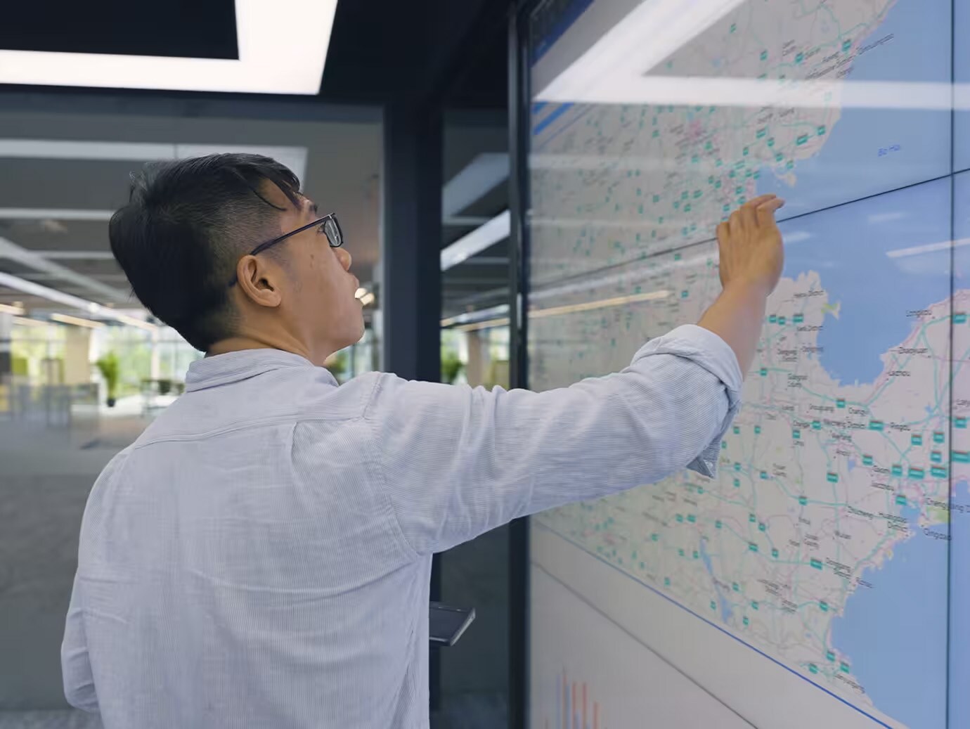 Man looking at a world map displayed on a large glass screen