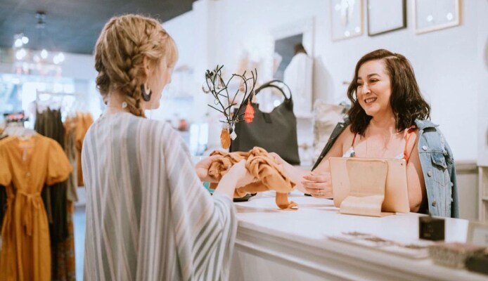 A female employee at a dress store's billing counter handing a dress to a woman