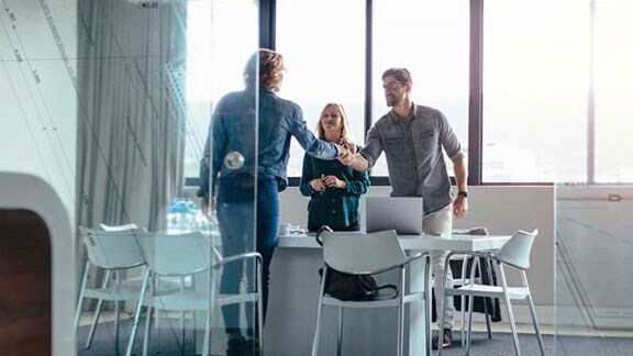 Man and woman smiling and shaking hands with a female client in a conference room