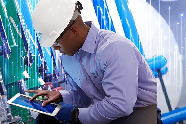 Man in Johnson Controls safety equipment using a tablet in front of machines with modern graphics