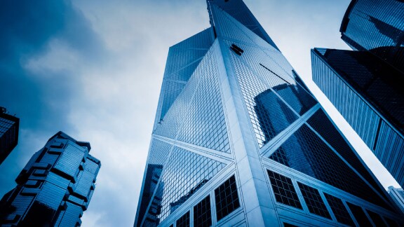 Upwards view of a skyscraper surrounded by smaller glass buildings against the sky