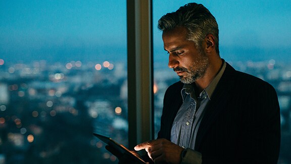 A businessman scrolling on a tablet by an office window