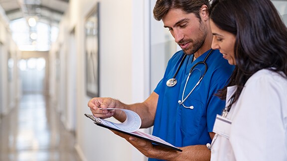 Two healthcare professionals in conversation, while one holds a clipboard