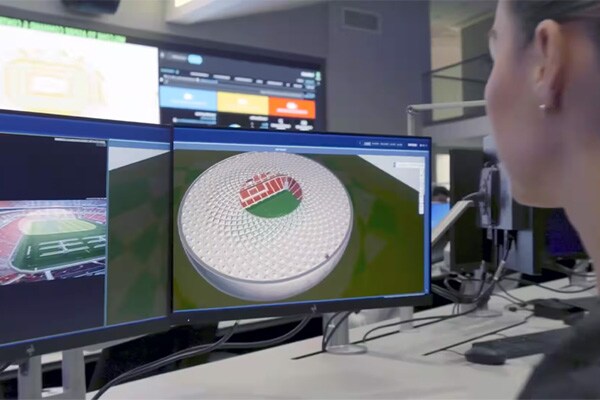 A person looking at a monitor displaying a 3D model of a stadium from the control room