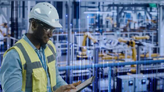 A worker looking at the readings on the tab while working on a factory overlaid with graphics of transmission nodes
