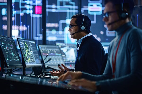 Two men wearing headphones working on codes displayed on their desktop